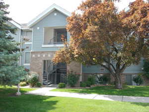 View of front of property with a balcony, brick siding, a front yard, and stairs