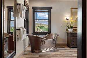 Full bath with vanity, a soaking tub, light wood-type flooring, and golf course view