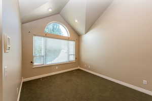 Spare room featuring dark carpet and vaulted ceiling