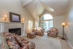 Living room with light colored carpet, a fireplace, beam ceiling, and high vaulted ceiling