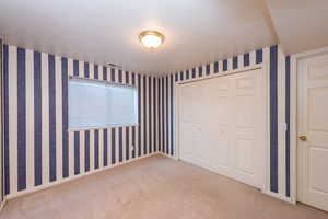 Unfurnished bedroom with carpet floors, wallpapered walls, a closet, and a textured ceiling