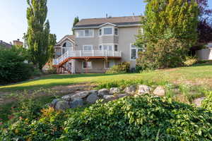 Back of property with a lawn, stairway, a wooden deck, and stucco siding
