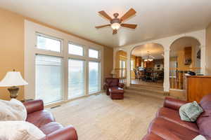 Carpeted living area featuring arched walkways, a chandelier, ceiling fan, and ornate columns