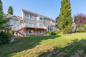 Rear view of property featuring a wooden deck, a lawn, stucco siding, and stairway