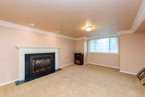 Unfurnished living room with carpet flooring, a fireplace with flush hearth, crown molding, and a textured ceiling