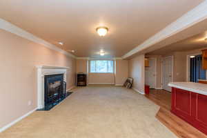 Unfurnished living room featuring a fireplace with flush hearth, ornamental molding, and light wood-type flooring