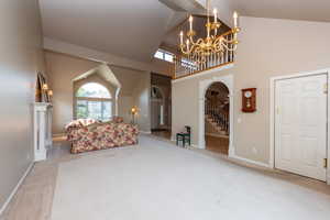 Living area featuring high vaulted ceiling, healthy amount of natural light, light carpet, stairway, and arched walkways