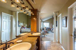 Ensuite bathroom featuring decorative columns, vaulted ceiling, double vanity, a textured ceiling, and light tile patterned floors