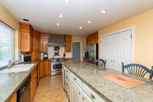 Kitchen featuring appliances with stainless steel finishes, wall chimney exhaust hood, recessed lighting, a breakfast bar area, and tasteful backsplash