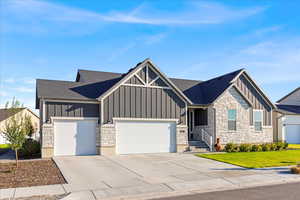 View of front of property featuring board and batten siding, stone siding, concrete driveway, a garage, and a shingled roof