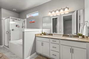 Full bath featuring double vanity, a shower stall, light marble finish flooring, and a garden tub