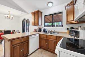 Kitchen with white appliances, a peninsula, brown cabinets, a chandelier, and light countertops