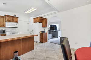 Kitchen with light countertops, brown cabinetry, arched walkways, and white appliances