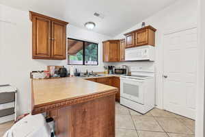 Kitchen featuring a peninsula, brown cabinetry, white appliances, lofted ceiling, and light countertops