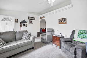 Carpeted living room featuring arched walkways, ceiling fan, and vaulted ceiling