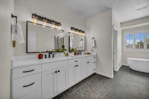 Bathroom with double vanity, a freestanding tub, dark tile patterned flooring, and a textured ceiling