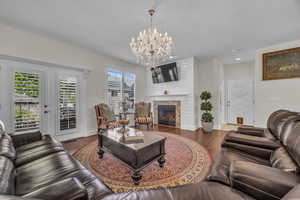 Living area with wood finished floors, a glass covered fireplace, a chandelier, recessed lighting, and french doors