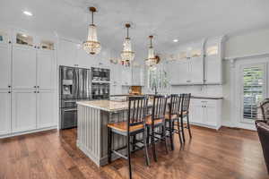 Kitchen with a kitchen bar, glass insert cabinets, a center island, appliances with stainless steel finishes, and recessed lighting