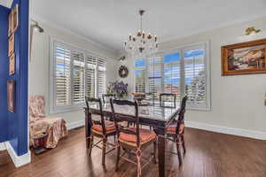 Dining area with crown molding, dark wood-style flooring, and a chandelier