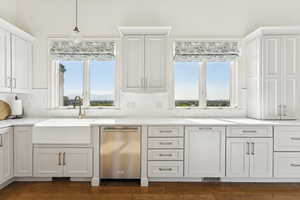Kitchen with white cabinets, decorative light fixtures, dishwasher, and light stone counters