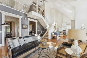 Living area with light wood-style flooring, high vaulted ceiling, stairs, a skylight, and a ceiling fan