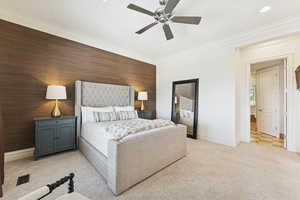Bedroom with ornamental molding, light carpet, a ceiling fan, and an accent wall