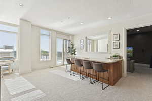 Bar area featuring light carpet, recessed lighting, brown cabinets, light stone countertops, and a textured ceiling