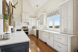 Kitchen with high vaulted ceiling, hanging light fixtures, light wood-type flooring, white cabinets, and tasteful backsplash