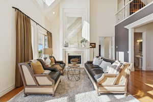 Living area with hardwood / wood-style floors, a high ceiling, a fireplace with flush hearth, and a skylight