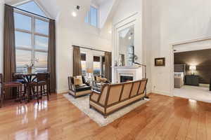 Living room featuring high vaulted ceiling, light wood-type flooring, a warm lit fireplace, and recessed lighting