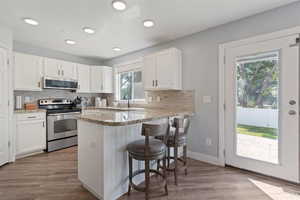 Kitchen featuring stainless steel appliances, white cabinetry, light stone countertops, a peninsula, and recessed lighting