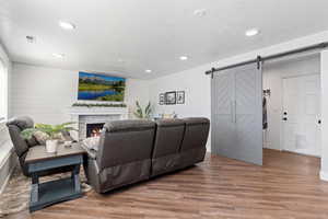Living area featuring light wood finished floors, recessed lighting, a barn door, wood walls, and a glass covered fireplace