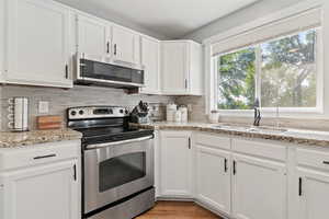 Kitchen with stainless steel appliances, white cabinets, backsplash, and light stone counters