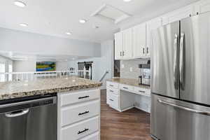Kitchen with appliances with stainless steel finishes, white cabinetry, dark wood-type flooring, light stone countertops, and recessed lighting
