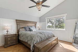 Bedroom featuring a decorative wall, light wood-type flooring, vaulted ceiling, ceiling fan, and a wainscoted wall