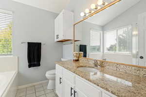 Bathroom featuring a bath, vanity, light tile patterned floors, and vaulted ceiling
