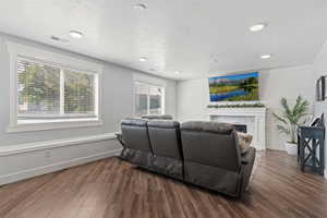 Living room with dark wood finished floors, a stone fireplace, recessed lighting, a textured ceiling, and wooden walls