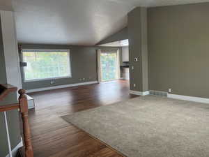Unfurnished living room featuring dark wood-style flooring, lofted ceiling, and a textured ceiling