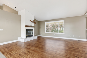 Unfurnished living room featuring vaulted ceiling, a fireplace, and wood finished floors