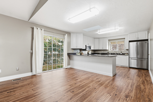 Kitchen with a peninsula, white cabinets, freestanding refrigerator, and dark wood finished floors
