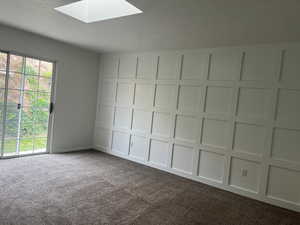 Unfurnished room with dark colored carpet, a skylight, a textured ceiling, and a decorative wall