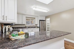 Kitchen with white cabinets, dark stone counters, appliances with stainless steel finishes, a peninsula, and a skylight