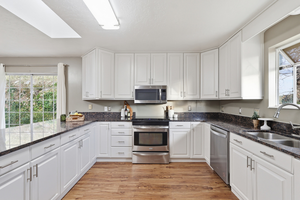 Kitchen featuring white cabinetry, dark stone countertops, appliances with stainless steel finishes, light wood-style flooring, and a skylight