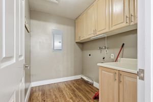 Washroom with cabinet space, electric panel, dark wood-style flooring, and hookup for an electric dryer