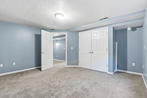 Unfurnished bedroom with a textured ceiling, light carpet, and a closet