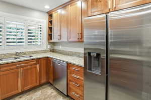 Kitchen with appliances with stainless steel finishes, open shelves, light stone counters, brown cabinets, and recessed lighting