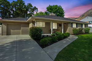 Ranch-style house featuring covered porch, an attached garage, a chimney, concrete driveway, and a shingled roof