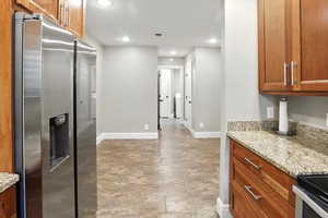 Kitchen with brown cabinetry, stainless steel fridge with ice dispenser, light stone counters, recessed lighting, and light stone finish floors