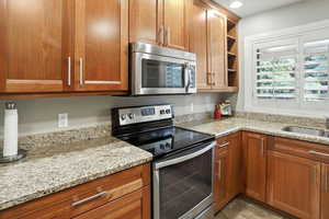 Kitchen with appliances with stainless steel finishes, light stone countertops, open shelves, brown cabinets, and recessed lighting