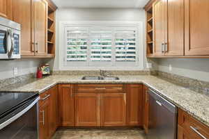 Kitchen with open shelves, stainless steel appliances, light stone counters, and brown cabinets